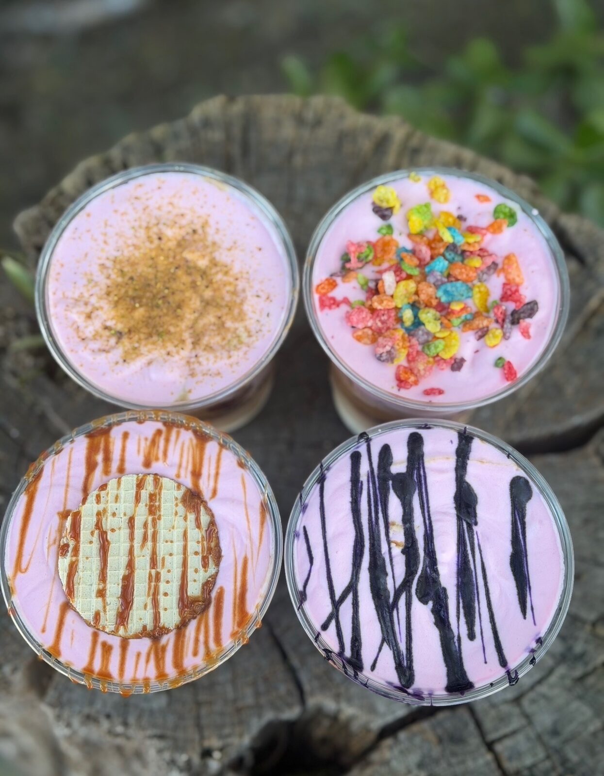 Four iced specialty lattes seen from above — pink cold foam with cinnamon, Fruity Pebbles, caramel drizzle and dark chocolate drizzle.
