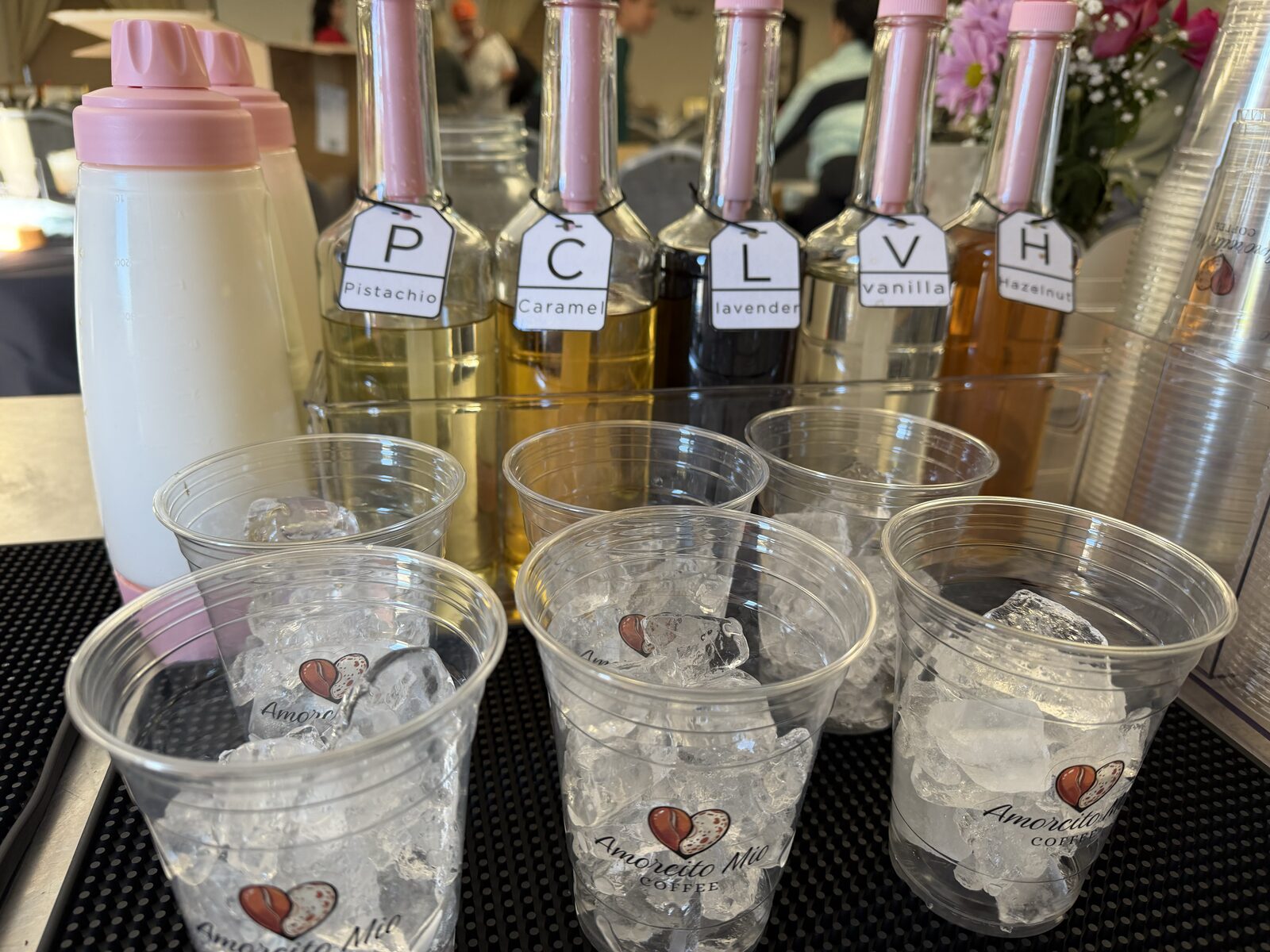 Glass syrup bottles with hand-lettered tags beside cups of ice at the cart.